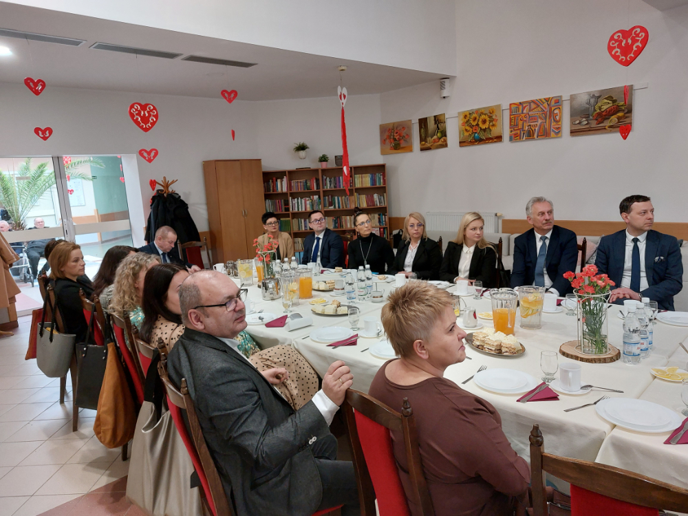 Zdjęcie przedstawia wnętrze Domu Pomocy Społecznej w Baszkowie Grupa osób na corocznym spotkaniu Zarządu Powiatu Krotoszyńskiego w osobach Starosty Krotoszyńskiego Stanisława Szczotki, Wice – Starosty Krotoszyńskiego Pawła Radojewskiego, Członka Zarządu – Miłosza Zwierzyka, Pani Sekretarz Powiatu – Joanny Dymarskiej – Kaczmarek z kadrą kierowniczą pomocy i integracji społecznej powiatu krotoszyńskiego Dyrektorzy PCPR, DPS w Baszkowie, DPS w Zdunach, ŚDS, WTZ przedstawili najważniejsze założenia w zakresie inwestycji i potrzeb wsparcia społecznego Wystąpienie Małgorzaty Nyczki Dyrektor ŚDS w Krotoszynie Pomieszczenie jest ozdobione dziełami sztuki na ścianach oraz małymi dekoracjami w kształcie serca wiszącymi z sufitu