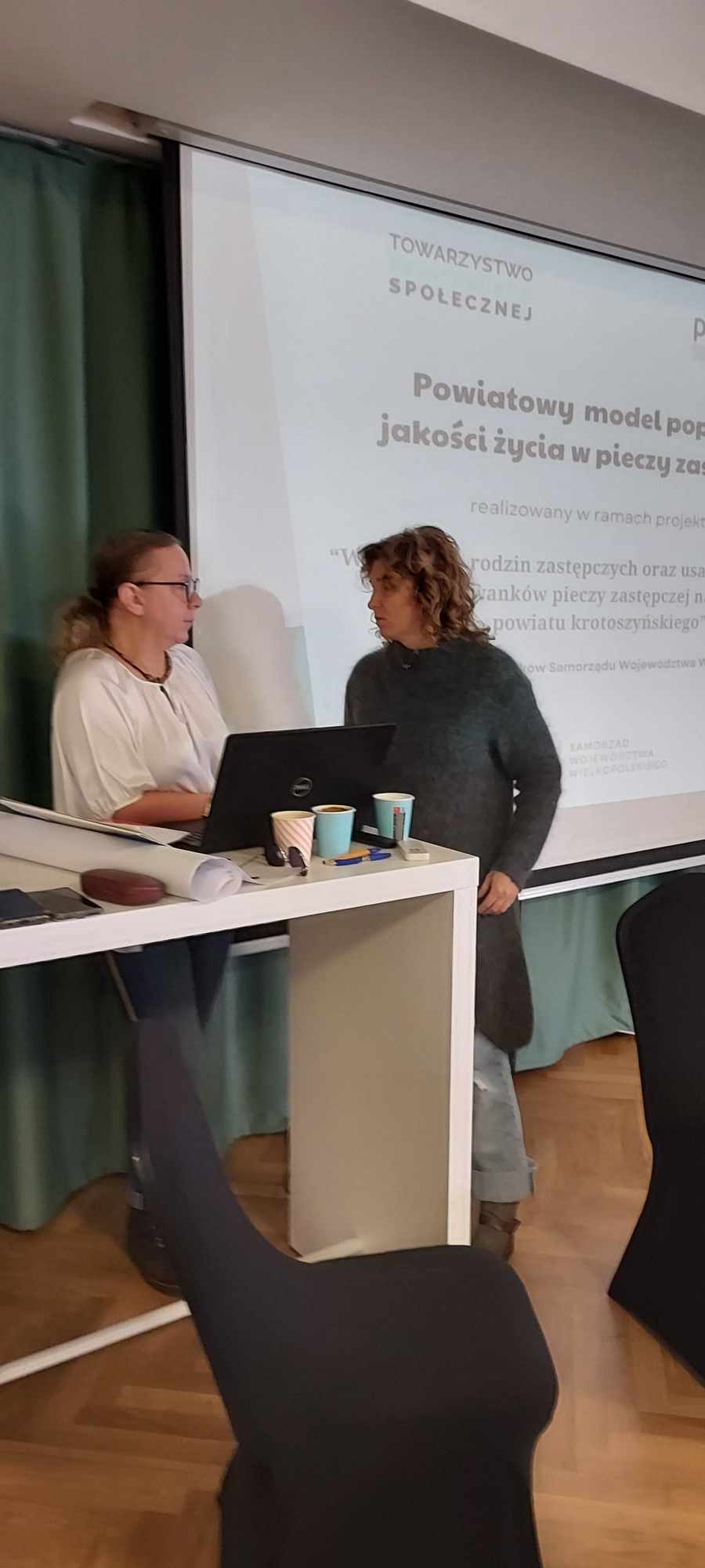 Zdjęcie ze spotkania przedstawiające osoby prowadzące przy laptopie na tle ekranu z prezentacją