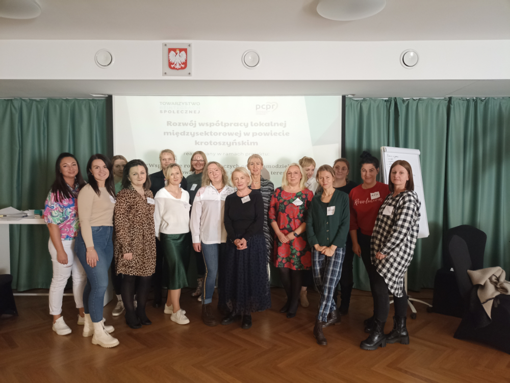 Zdjęcie grupowe na tle ekranu ze slajdem uczestników szkolenia "Rozwój współpracy lokalnej międzysektorowej w powiecie krotoszyńskim"